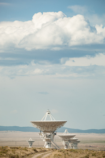 telescope satellite dishes amongst the desert mountain landscape and cloud filled sky.  the very large array, socorro, new mexico.