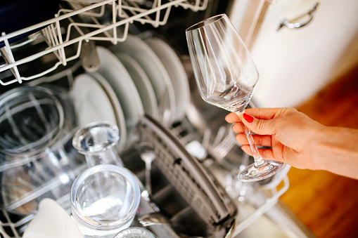 Close up image of a young woman's hand taking a clean wine glass out of the dishwasher machine in her apartment in Paris, France. House work, domestic work concepts in a modern, French kitchen.