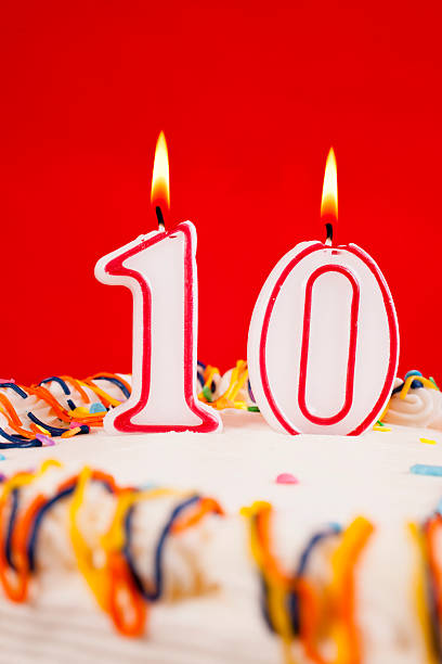 istock Decorated birthday cake with number 10 lit candles.  Red background. 537485971