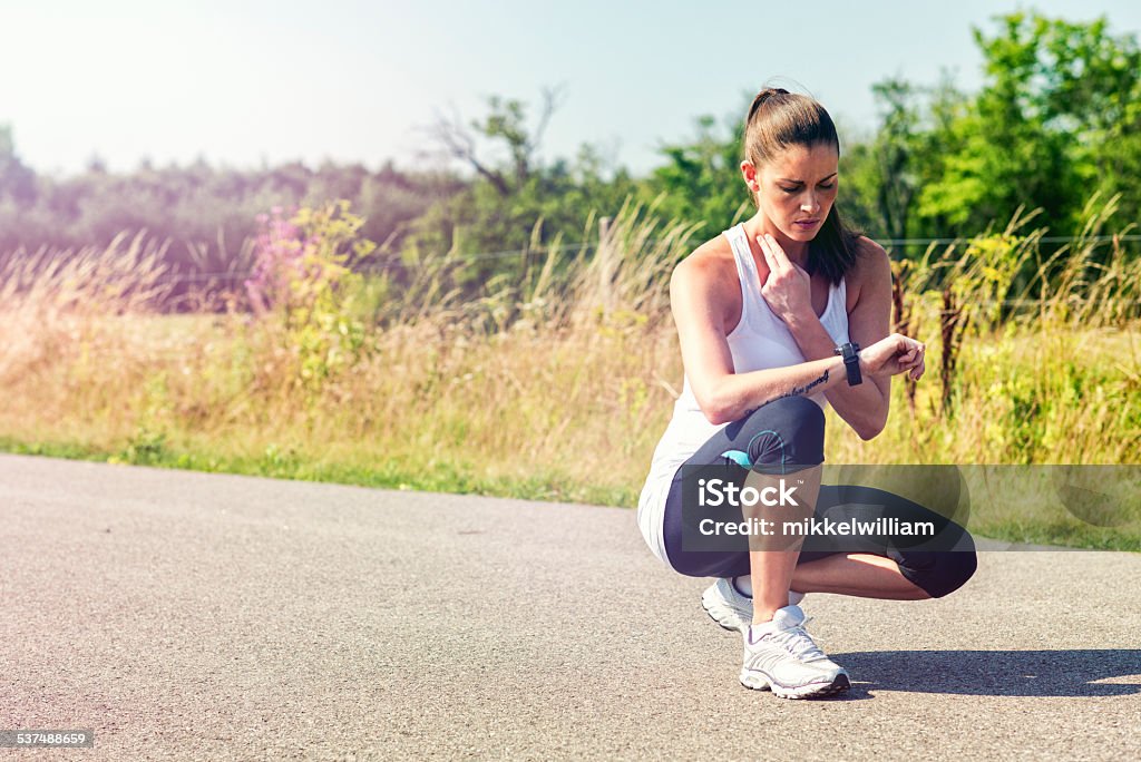 Female runner takes a break and measure pulse Woman has been running and sits down. She is measuring her pulse while looking at her sports watch. 20-29 Years Stock Photo