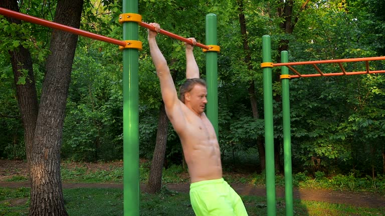 Sports lifestyle, street workout. Muscular man performing an exercise for the torso on the bar. Outdoor sports ground