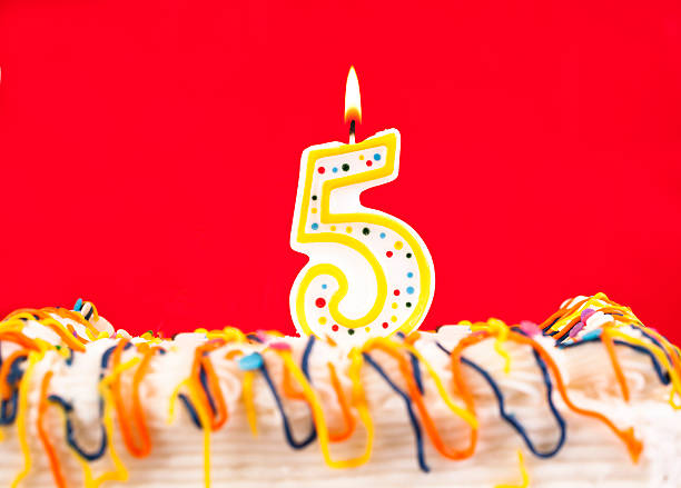 istock Decorated birthday cake with number 5 lit candle.  Red background. 537499221
