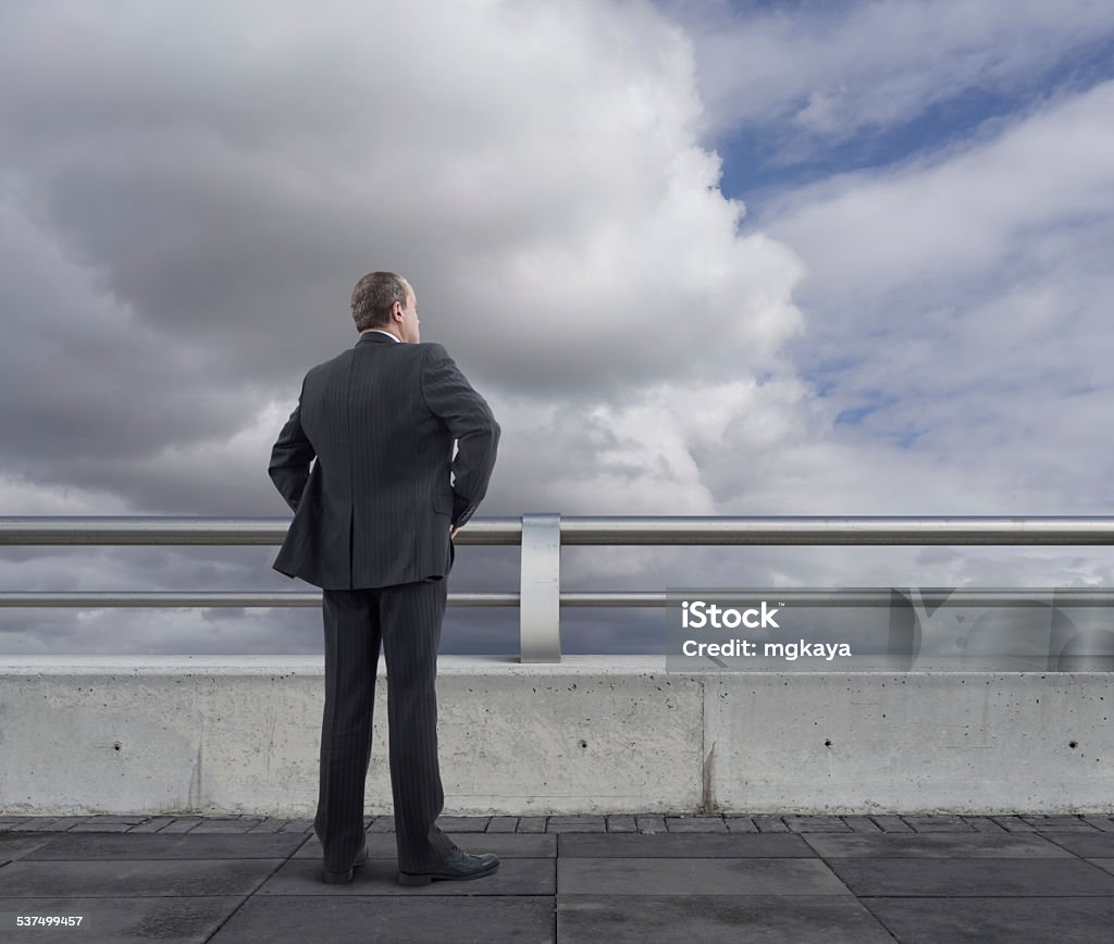 Businessman on the Bridge Rear view of businessman standing and looking on the bridge (or rooftop) with cloudy sky background. He is looking further, thinking and searching new ideas. 2015 Stock Photo
