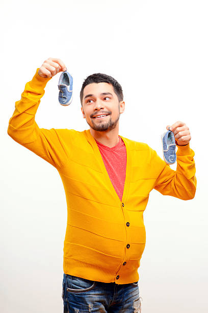 What if men could bear children. Funny conceptual photo of gender reversal when a pregnant man with a belly holding baby shoes while posing isolated on white background