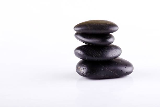 Horizontal photo of black lava stones. Black stones stacked at each other. Few stones on white board. Relaxing lava stones placed isolated on white background.