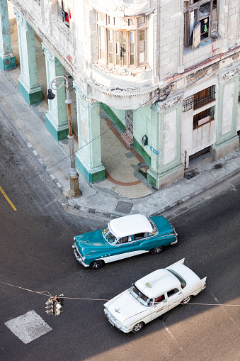 Vintage American cars driving through the streets in Havana Vieja, Cuba. Dilapidated buildings in traditional colonial style are visible in the background, 50 megapixel image.