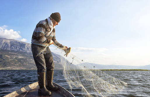 Old fisherman is catching fish with fishing net on his boat, Çivril, Denizli, Turkey.
