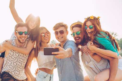 Group of young people on the beach having party. Taking selfie and dancing. They are happy and joyful. Sunny day.