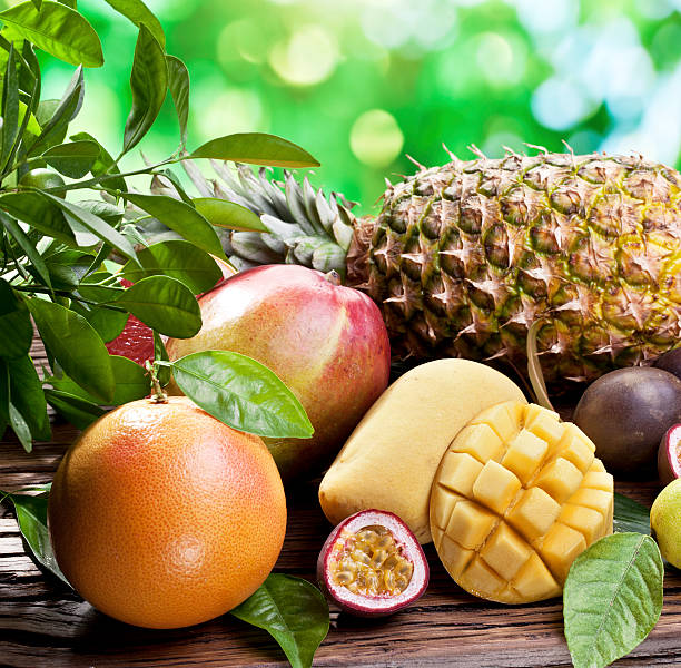 Exotic fruits on a wooden table with green foliage on the background.