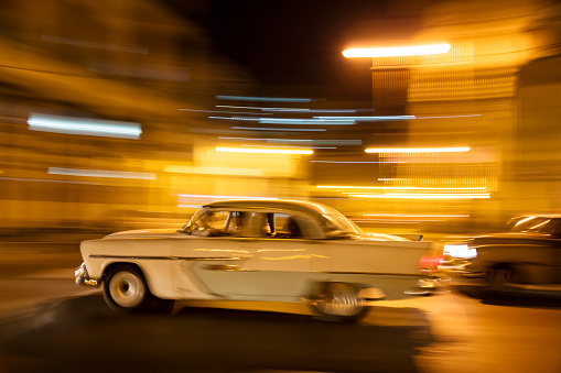 Vintage American car travels in motion blur through the dark streets of Havana, Cuba at night.