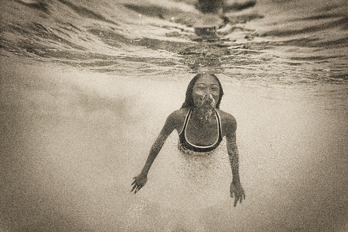 Serene image of a young Asian woman swimming alone underwater.