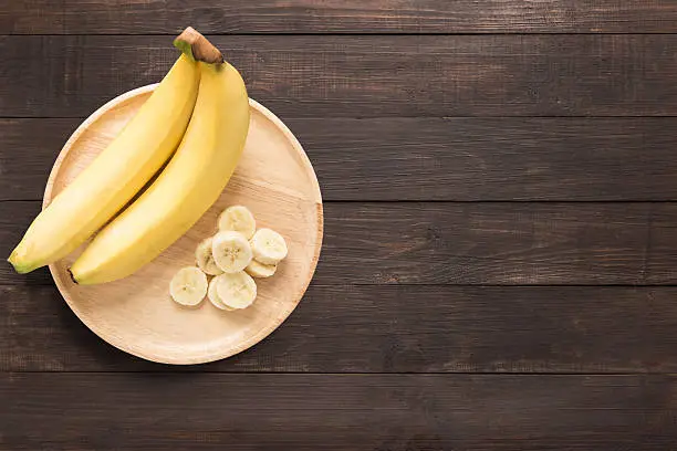 Photo of Bananas in a wooden dish on a wooden background.