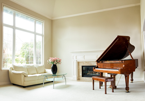 Living room with grand piano, fireplace, sofa and large window with bright daylight coming through.