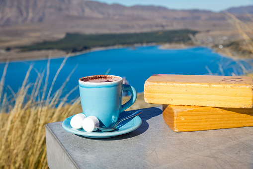 cup of hot chocolate with marshmallow on cement table with Lake Tekapo view