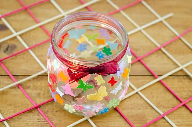 DIY candleholder decorated with colorful butterflies on a wooden table