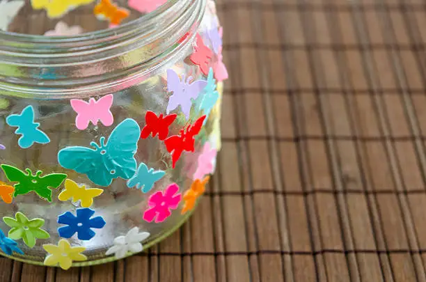 Closeup of a DIY candleholder decorated with colorful butterflies on a wooden table