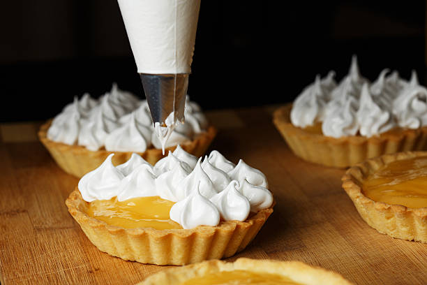 Delicious lemon curd tartlets  with meringue on wooden  table A process of decorating lemon tartlets with meringue icing meringue stock pictures, royalty-free photos & images