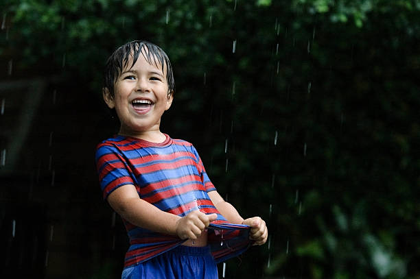 Child playing in the rain and drinking rainwater .
