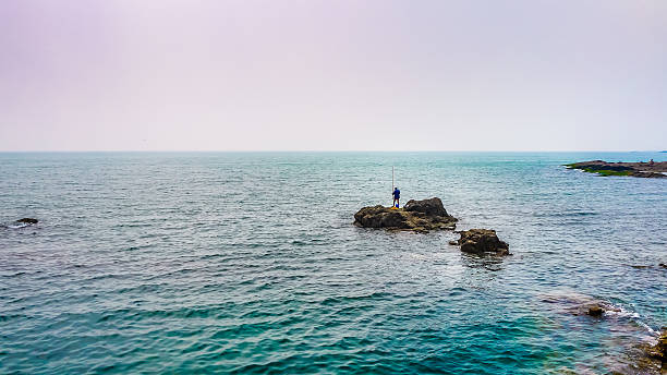 Tel Aviv/Israel-10/10/18: man fishing with a fishing rod on the breakwater near the lighthouse in Tel Aviv Marina on the sunset
