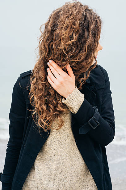 istock Curly brunette in black coat on the coast 537543614