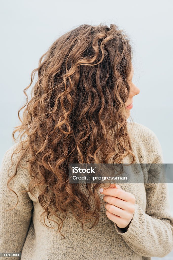 Curly brunette in a sweater on the coast Curly brunette in a sweater on the coast holding hair with her hand Women Stock Photo