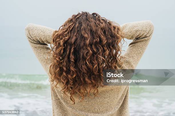 Curly Brunette In A Sweater On The Coast Stock Photo - Download Image Now - Curly Hair, Women, Rear View