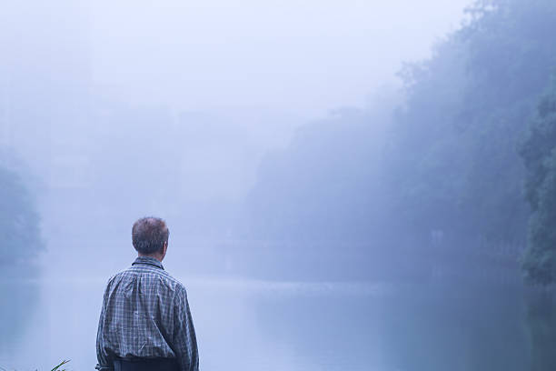 istock old man standing infront of lake in the mist 537544288