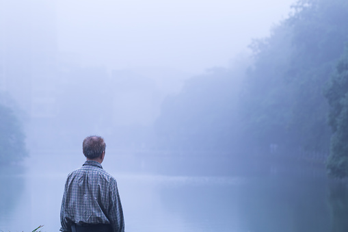 old man standing infront of lake in the mist alone