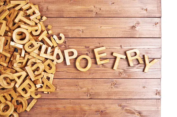 Word poetry made with block wooden letters next to a pile of other letters over the wooden board surface composition