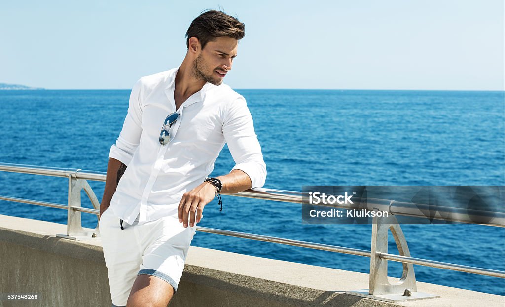 Hombre Guapo posando en ropa blanca usando un escenario al mar - Foto de stock de Hombres libre de derechos