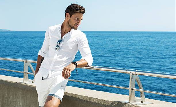 handsome man wearing white clothes posing in sea scenery - men's fashion stockfoto's en -beelden