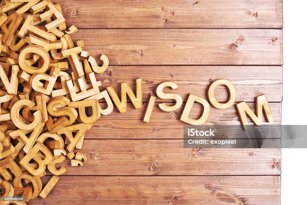 Word wisdom made with wooden letters Word wisdom made with block wooden letters next to a pile of other letters over the wooden board surface composition Abstract Stock Photo