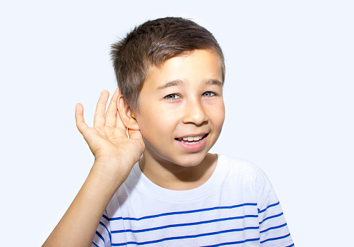 Portrait of happy little boy cupping his ear with his hands over colored background. Horizontal composition. Studio shot. Cute little boy putting his hand around his ear and listening over isolated on gray. Taken on gray background.