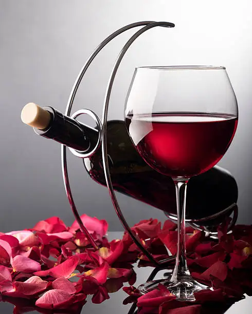 Composition of red wine glass, bottle of red wine, rose-petals