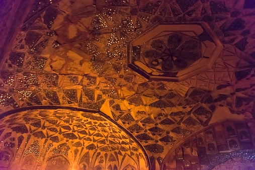 Interior decorative ceiling of Jasmine Palace dome. Gold and dark brown in color, with central floral motif. The upper portion of the supporting arches partially showing at the bottom of the picture.