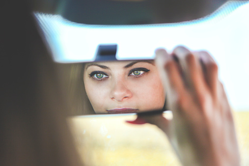 Young beautiful female driver with green eyes looking at herself in rearview mirror. 