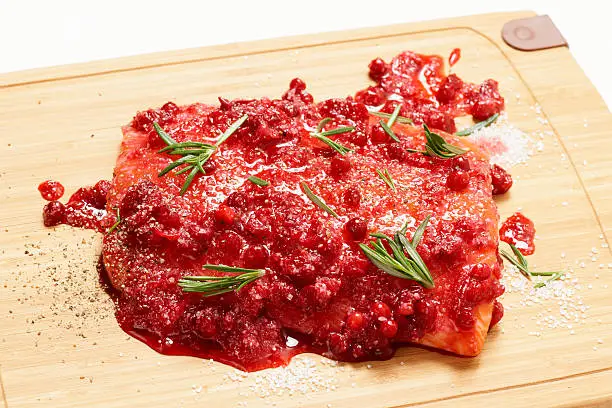 Salmon steak being marinated in salt with rosemary and redberries