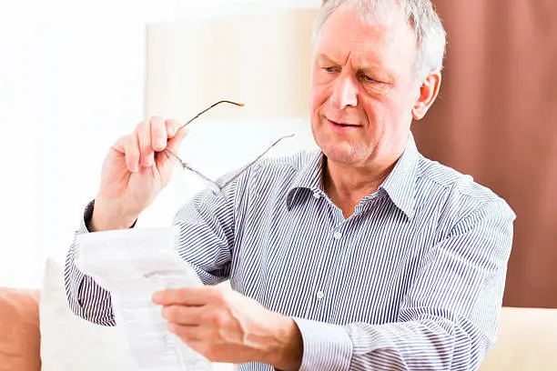 Old man reading  medicament package insert at home with glasses