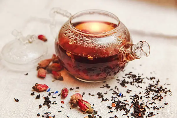 The Dry Red Small Roses with Black Tea in the Glass Teapot,Tea Drinking,Aromatized Flowers, Linen Tableclose;Toned