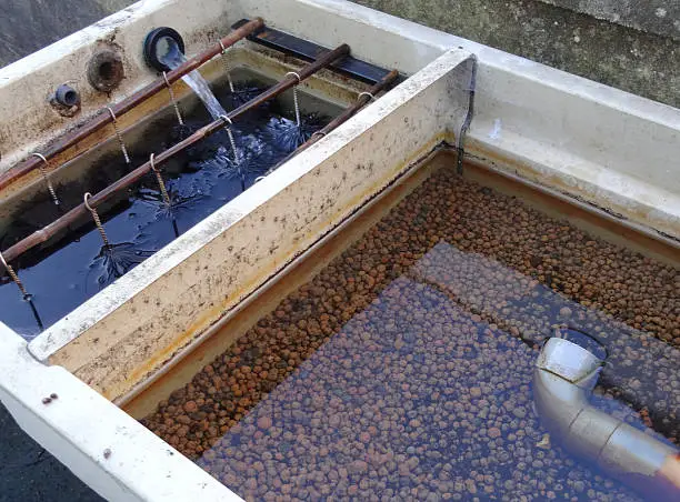 Photo showing a small garden pond filter, consisting of two chambers - brushes and Japanese matting, and pea gravel / lytag.  This filter is necessary to maintain the water quality adjacent pond, so that the goldfish and koi carp will thrive and grow, enjoying clear, purified pond water.