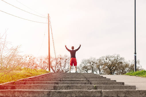 Man holding arms up in success gesture at the top of stairs in a park