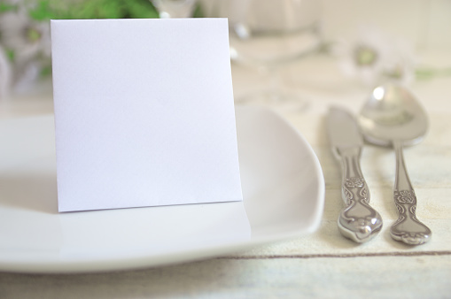 Invitation card on a decorated table with classic cutlery and some flowers.