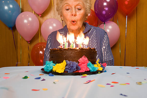 年配の女性がケーキの上のろうそくを吹き - cake birthday candle blowing ストックフォトと画像