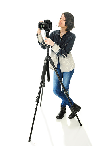 An attractive young teen photographer adjusting the camera on her tripod.  On a white background.