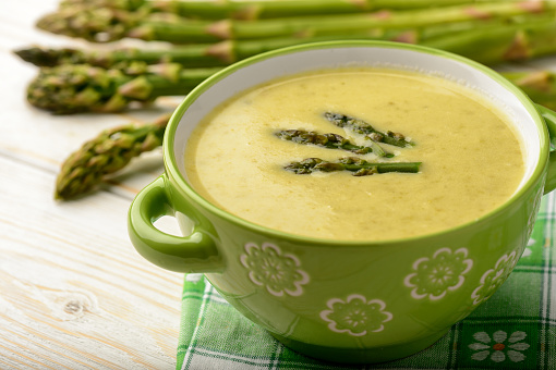 Green asparagus cream soup on wooden background.