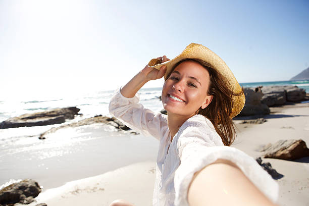 despreocupada mujer de vacaciones en la playa tomando autofoto - women relaxation tranquil scene elegance fotografías e imágenes de stock