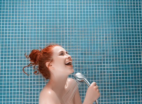 young woman with happy attitude washing herself in the shower, smiling and relaxing, singing her favourite song,