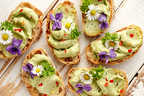 Canapes with avocado paste and edible flowers Delicious canapes with avocado paste and edible flowers on wooden background edible flower stock pictures, royalty-free photos & images