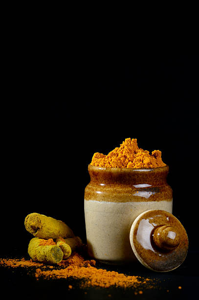 polvere di curcuma con radici o cortecce su sfondo nero - spice ayurveda herb curry powder foto e immagini stock