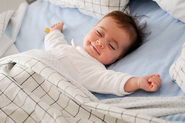 Smiling baby girl lying on a bed Smiling baby girl lying on a bed sleeping and smiling on blue sheets cute baby laughing stock pictures, royalty-free photos & images
